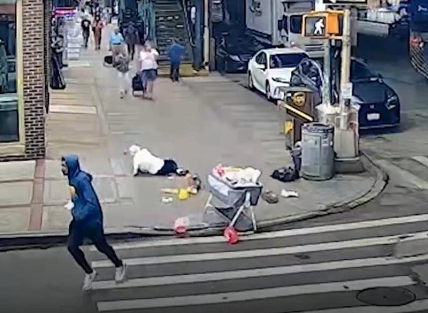 A person in a blue hoodie runs across a crosswalk while a baby lies next to a high chair on the sidewalk.