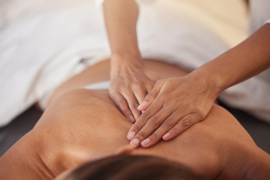 A massage therapist's hands massaging the upper back of a person lying face down.