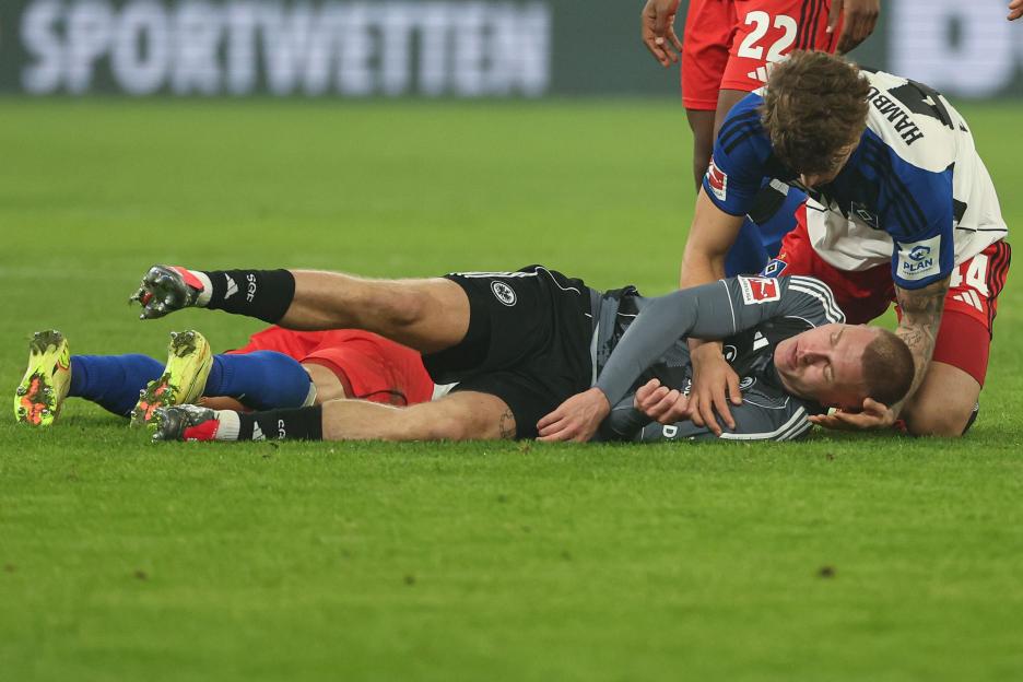 Eintracht Frankfurt player lies injured on the field while a Hamburger SV player kneels beside him.
