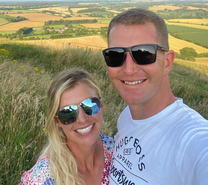 Georgie Campbell and a man pose for a selfie with a scenic landscape behind them.