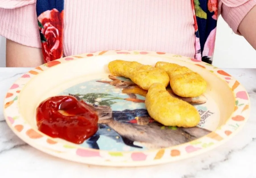 A child holding a plate of Turkey Twizzlers and ketchup.