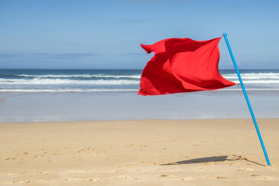 Red warning flag on an empty sandy beach with waves in the background.