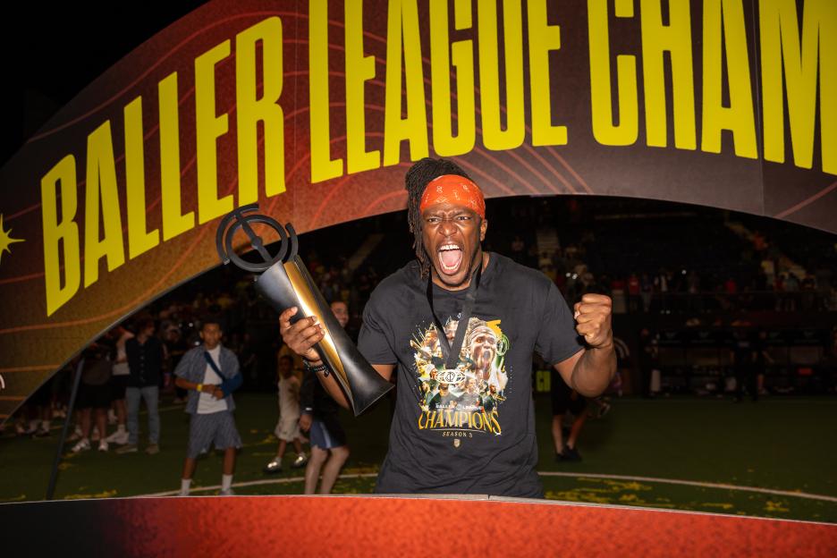 KSI, wearing a red bandanna, screams in celebration while holding the Baller League trophy.