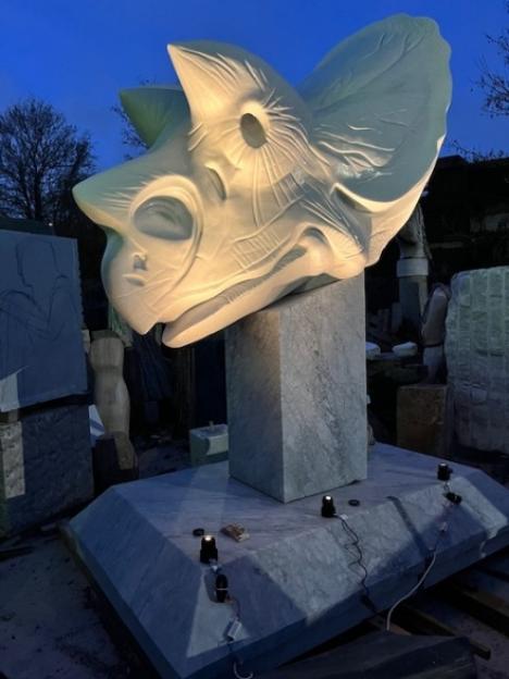 Sculpture of a stylized dinosaur head, possibly a Triceratops, illuminated from below.