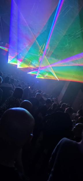 A crowd of clubbers at a rave with rainbow-colored laser lights shining above them.