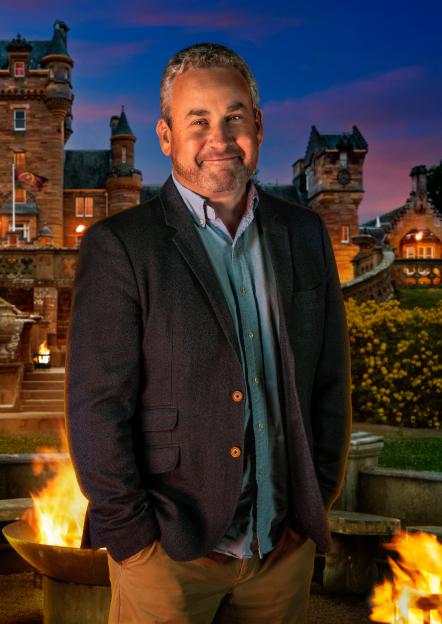 Hugo, a 51-year-old barrister, stands with a fire pit in front of a castle.
