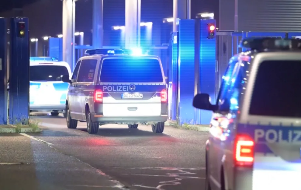 German police vehicles with flashing blue lights outside Leipzig Airport at night.