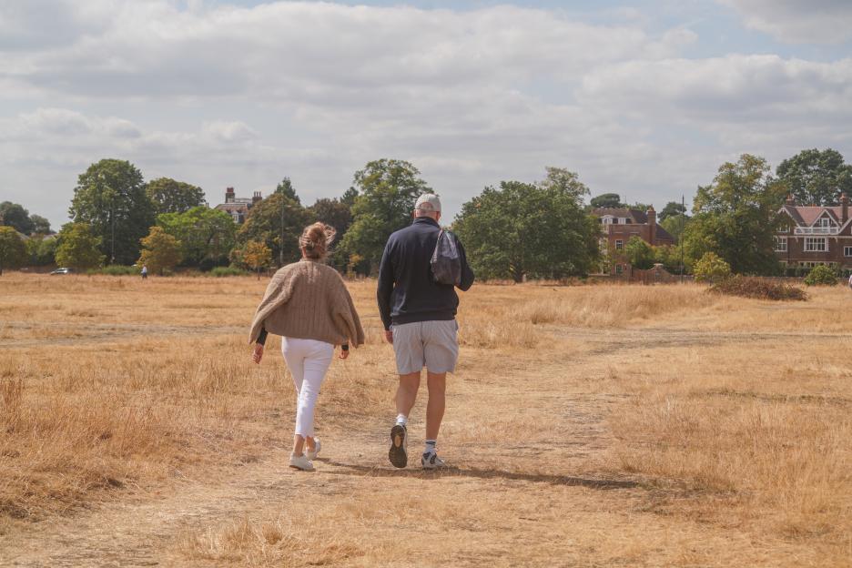 Two people walk across a field of scorched, dry grass at Wimbledon Common.