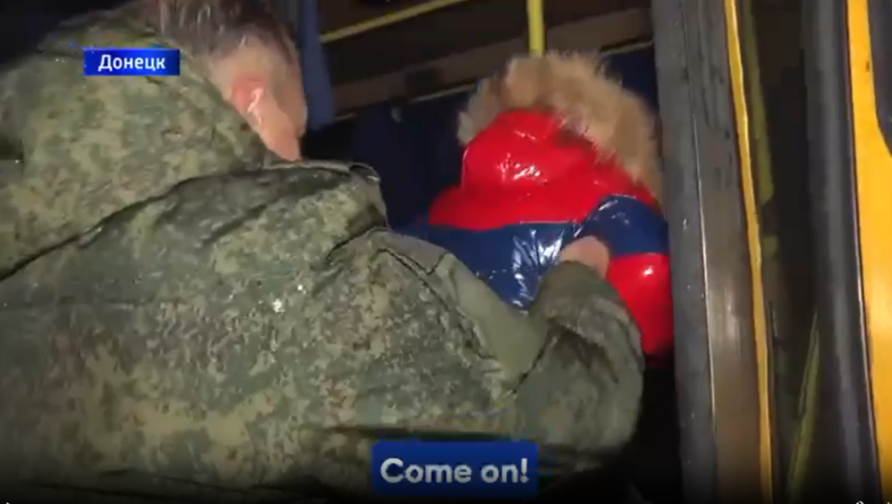 A person in a military uniform pulling a child in a red and blue jacket into a vehicle.