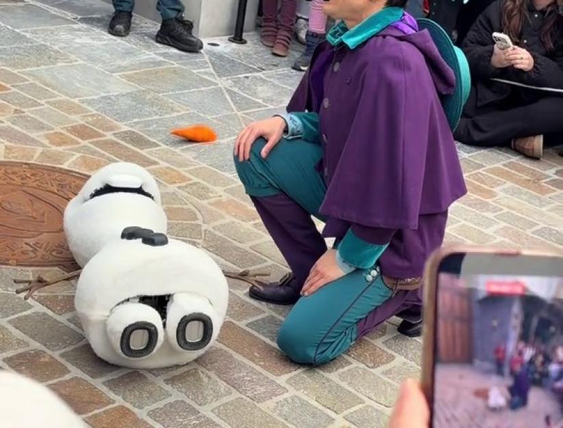 An Olaf robot has fallen over on the ground as people film and watch in disappointment.