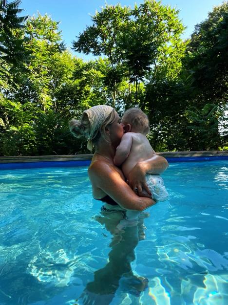 Emily Atack holding her baby Barney in a pool, with trees in the background.