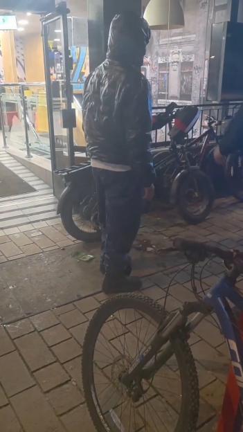 Person wearing a hooded jacket standing near a delivery vehicle and a bicycle.