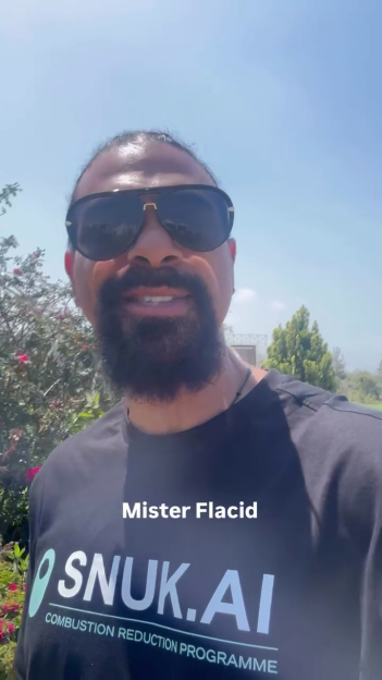 A man with sunglasses and a beard wearing a black t-shirt with "SNUK.AI COMBUSTION REDUCTION PROGRAMME" and "Mister Flacid" written on it.