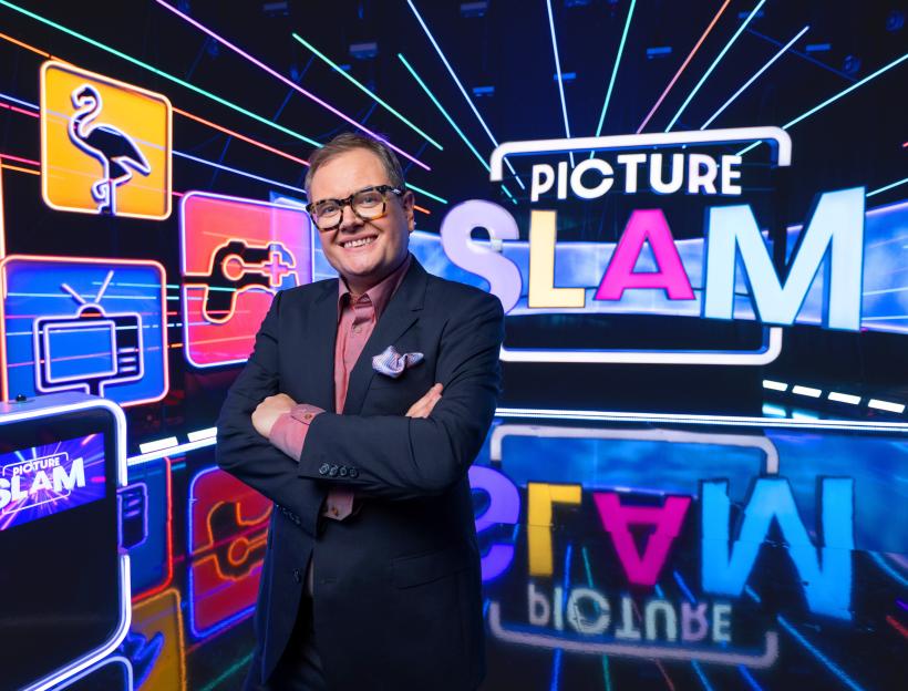 Alan Carr stands smiling in a studio with the "Picture Slam" logo and neon image icons.
