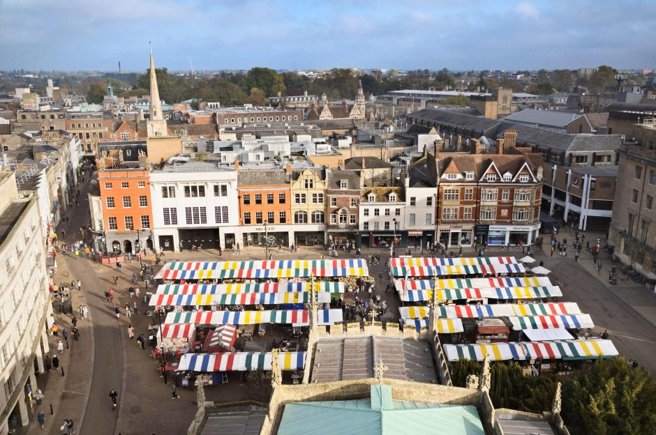 Aerial view overlooking the Cambridge market square with many colorful striped market stalls and historic buildings in England.