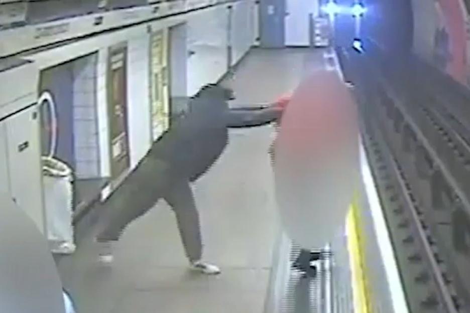 A person in dark clothing reaching to push an object, possibly another person, onto subway tracks as a train approaches.