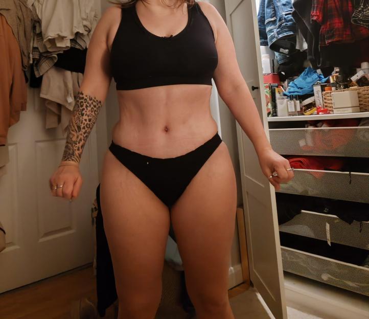 A woman in black underwear showing her stomach with a leopard print tattoo on her arm.