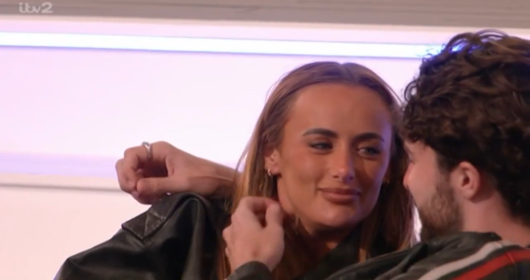 A woman in a black leather jacket smiling at a man in a black and red jacket.