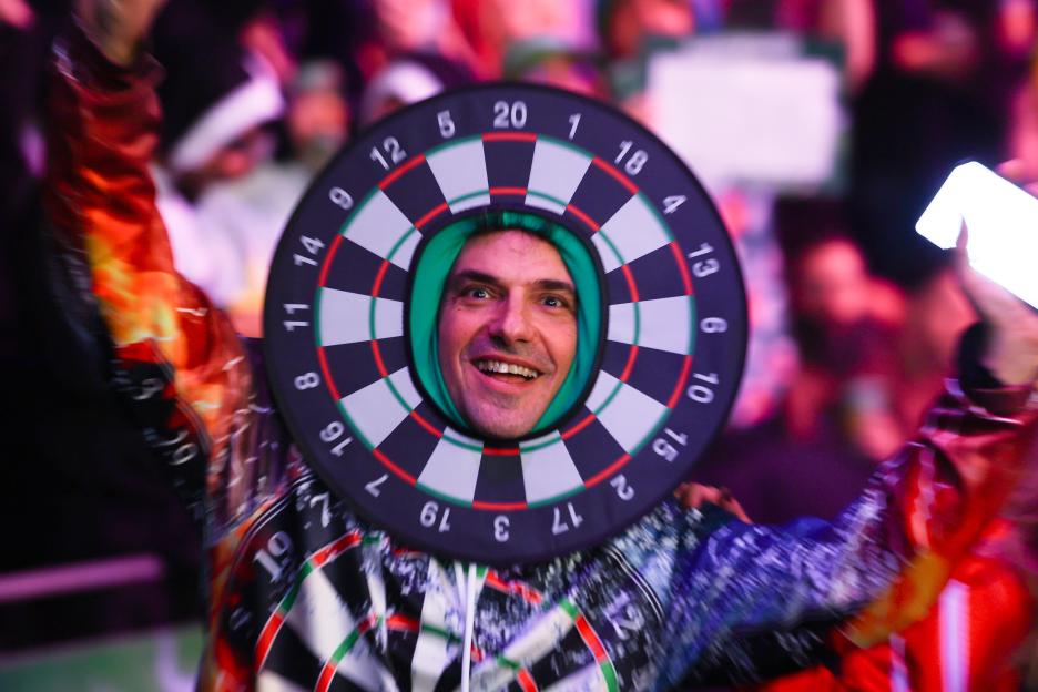 A man smiling with his face in the center of a dartsboard.