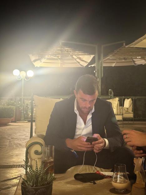 Fabrizio Romano looking at his phone at an outdoor restaurant.