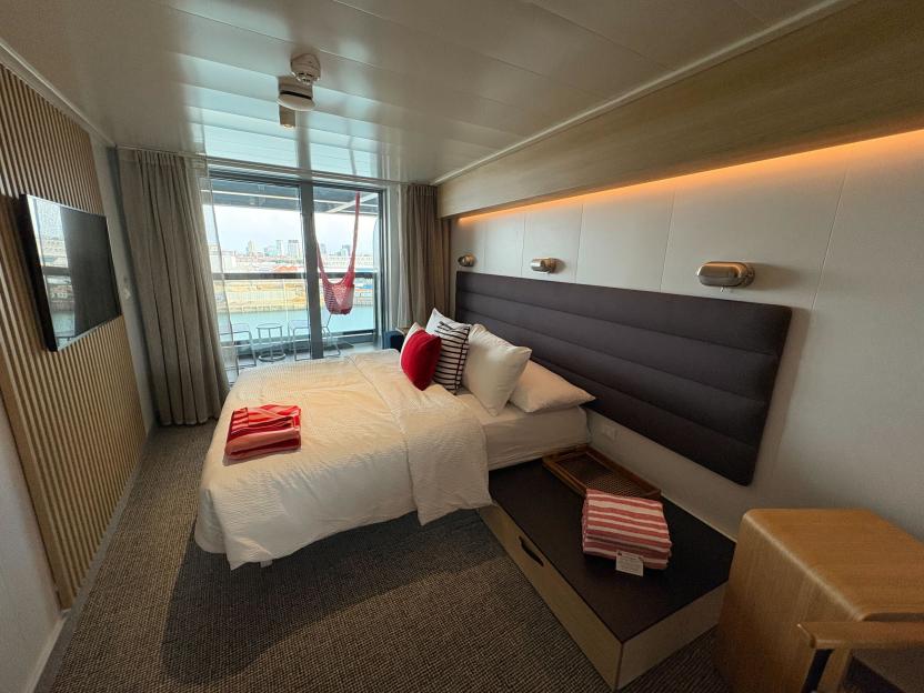 Cruise ship cabin with bed, balcony, and hammock.