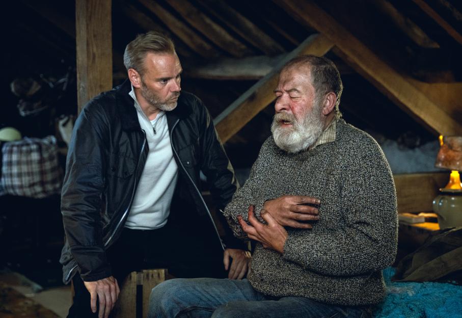 Joshua Richards as Bear Wolf and another man, in a dark setting, looking distressed with blood on his arm.