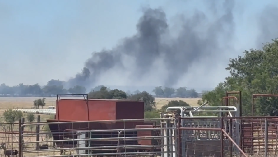 Dark smoke rising from fires in a rural field.