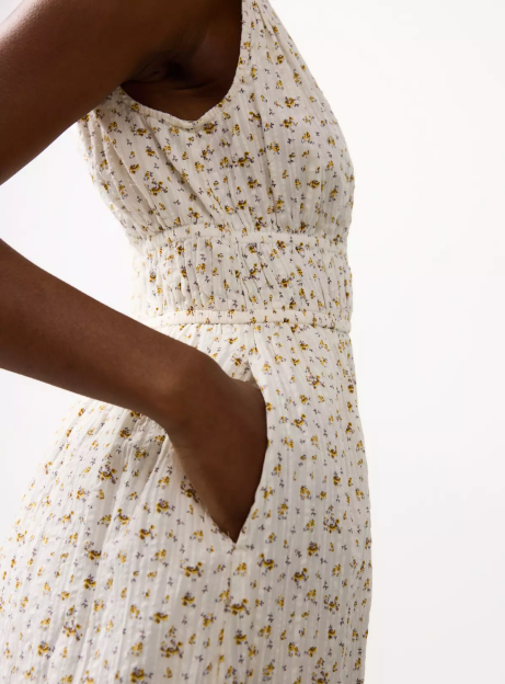 Close-up of a person's hand in the pocket of a white floral dress with yellow flowers.