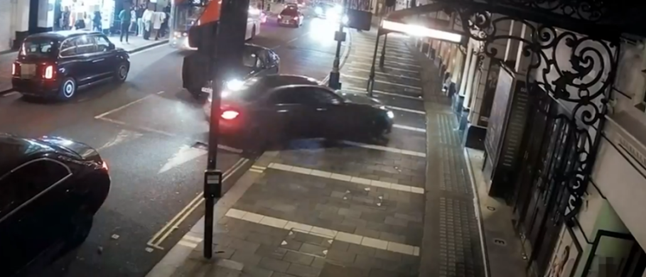 A black car driving over a curb and onto the sidewalk.
