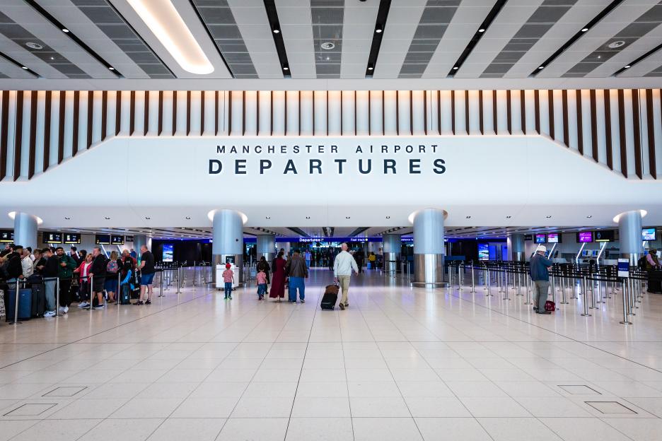 Travelers walking through the Manchester Airport Departures lounge.