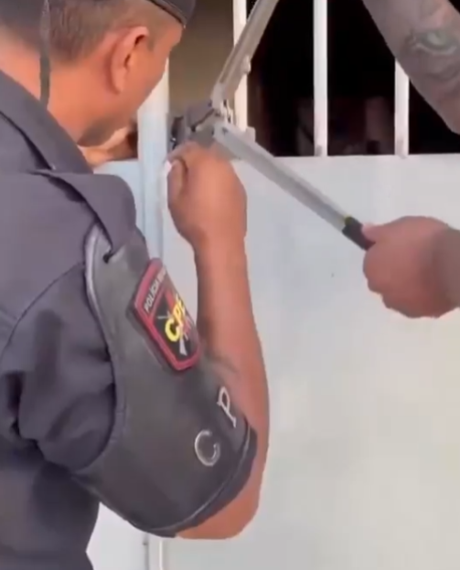 A police officer uses a bolt cutter on a gate.