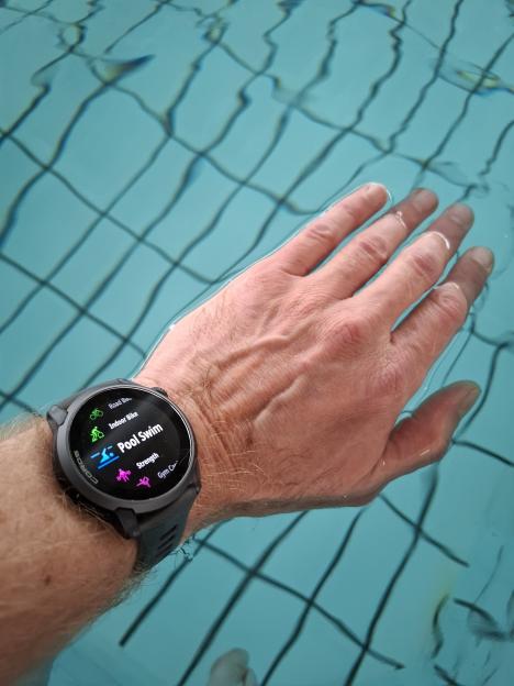 A hand submerged in water with a Coros watch displaying "Pool Swim" mode.