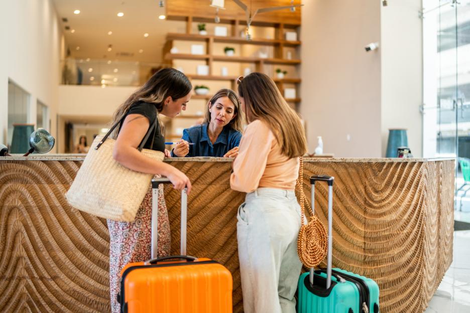 A hotel receptionist assists two women with their luggage at the front desk.