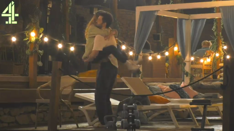 A man lifts a woman into his arms in an outdoor, string-light-lit setting.