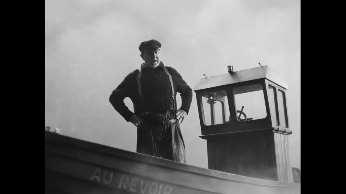 Ted Lasso standing with hands on hips on a boat with "AU REVOIR" written on the side.