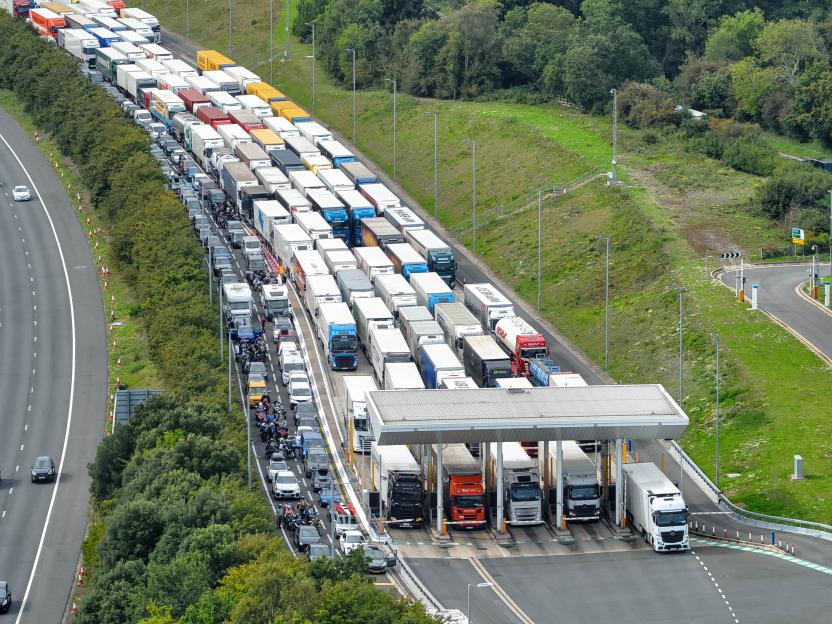 An aerial view of a long line of trucks, cars, and motorcycles waiting at toll booths for the Channel Tunnel.