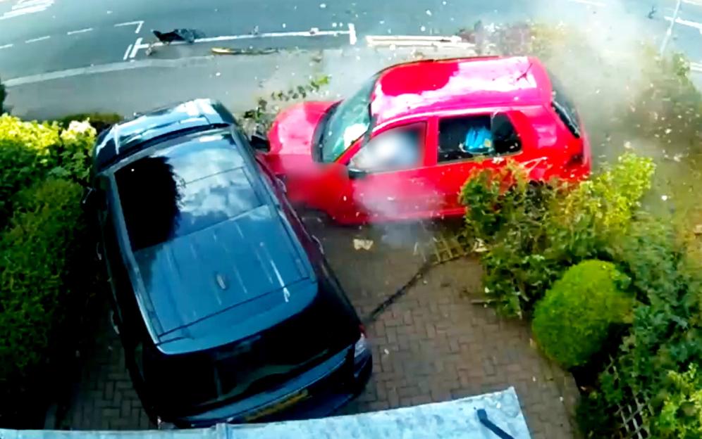 A red car crashed into the front garden, damaging a black car.