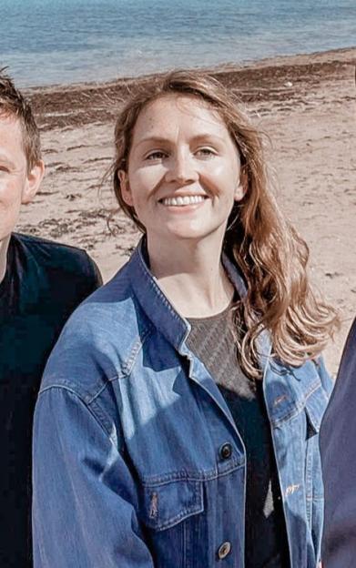 Four people smile at the camera while standing on a beach with the ocean behind them.
