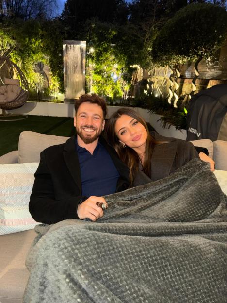 Sam Thompson and his new girlfriend on a couch under a blanket.