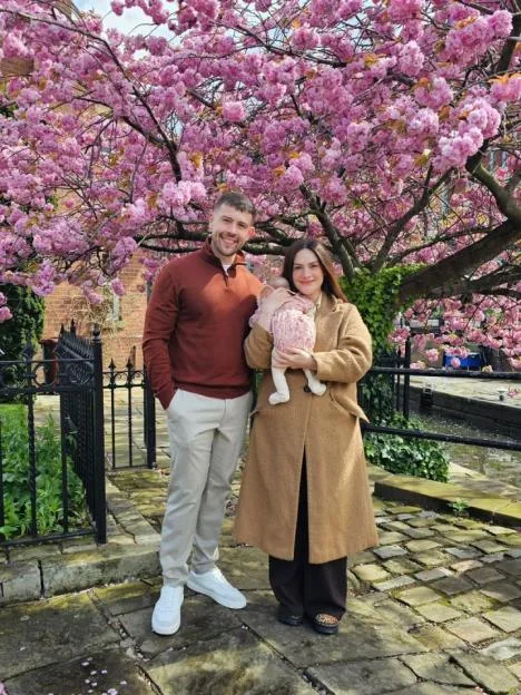 Isabel Hodgins standing with her partner and baby beneath a blossoming cherry tree.