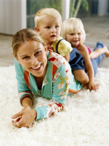 Two girls (21-24 months) on woman's back, lying on rug, smiling