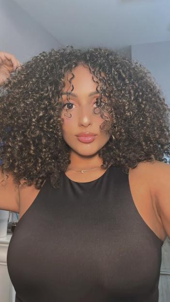 Daniella Abreu with long curly brown hair, wearing a black top and a gold necklace with a small pendant.