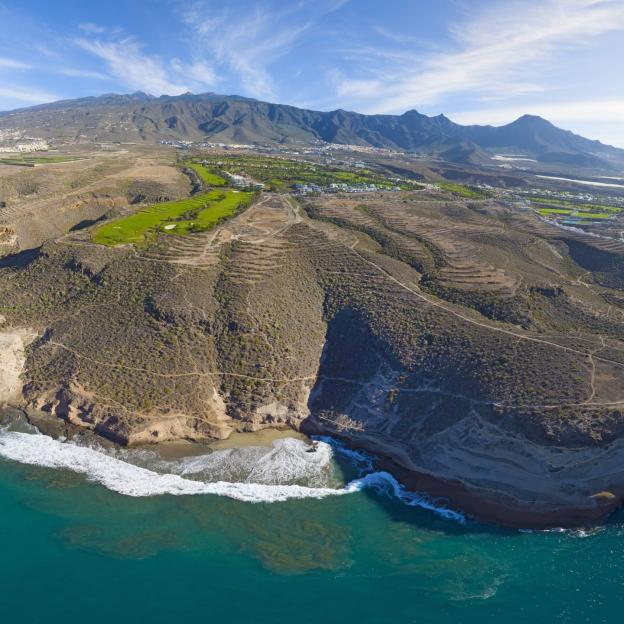 Aerial view of Golf Costa Adeje in Tenerife, showing green golf courses, coastal cliffs, and the ocean.