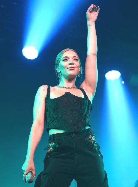 Becky Hill performing on stage at Heaven, with her right arm raised.