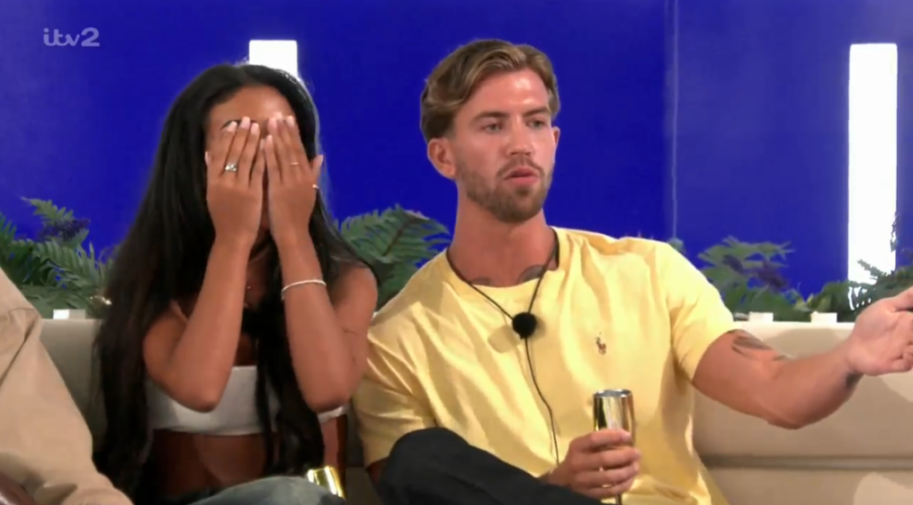 A woman covering her face and a man gesturing while holding a glass.