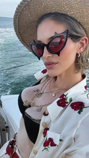 Kelly Osbourne on a sunny getaway wearing a straw hat, cat-eye sunglasses, and a floral shirt.
