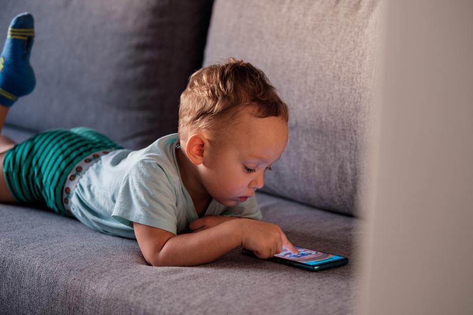 A young boy playing a mobile game on a smartphone while lying on a sofa.