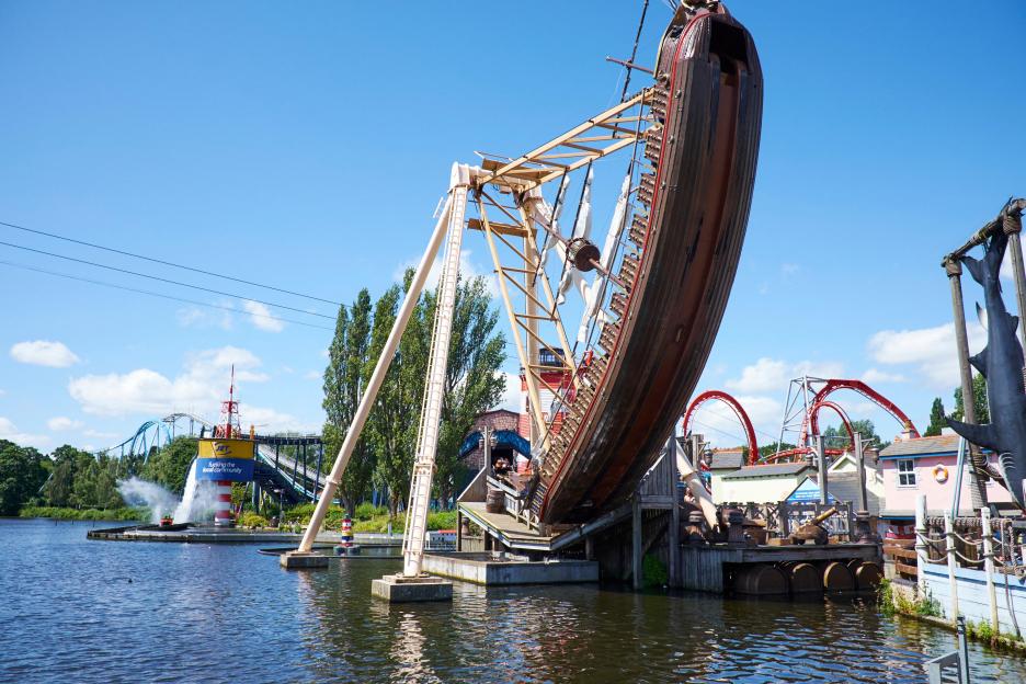 Pirate Ship ride at Drayton Manor Theme Park with a blue and red lighthouse and water ride in the background.