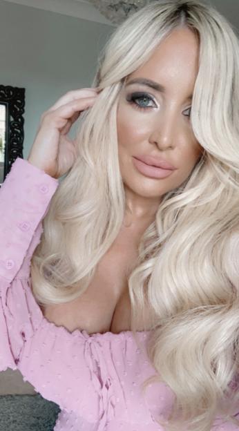 Woman with long blonde hair, full lips, and heavy eye makeup, wearing a pink dress.