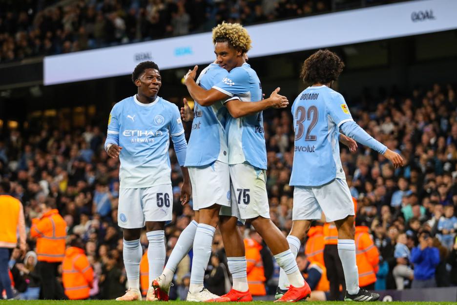 Three Manchester City players in light blue jerseys celebrating on the field.